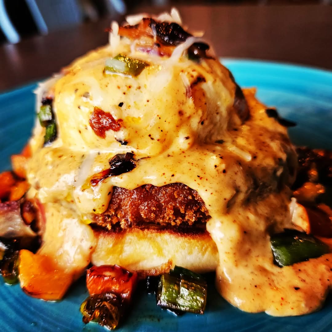 A crab cake Benedict under hollandaise on a blue plate, over roasted peppers and onions, at Jo Jo Macs.