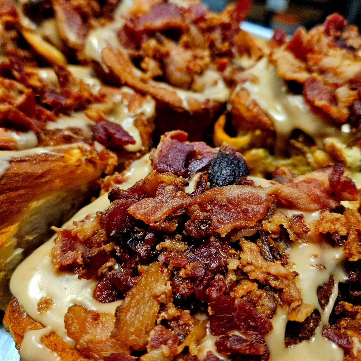 A tray of bacon-topped cinnamon rolls under maple glaze from The Original Cinn.